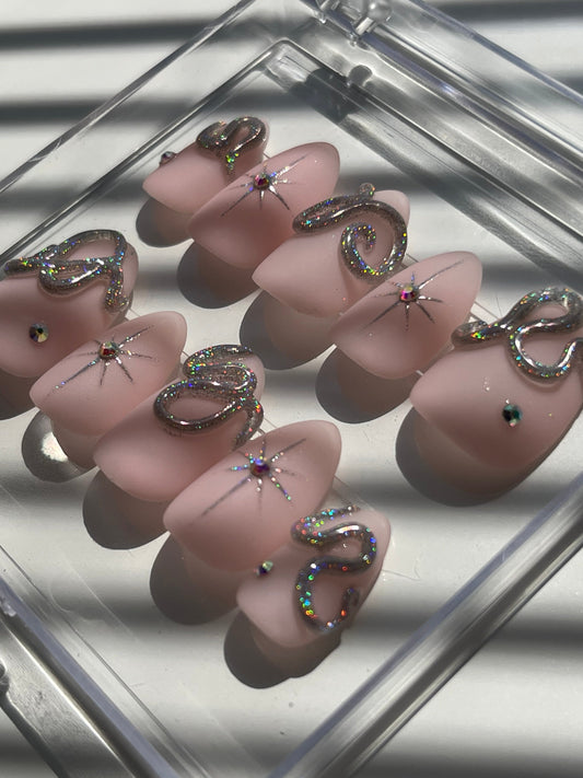 Set of pink nail art designs with decorative elements on a clear stand.