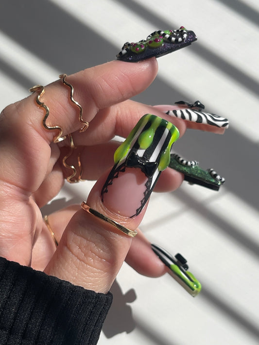 Hand with green and black nail polish holding a small object against a white background