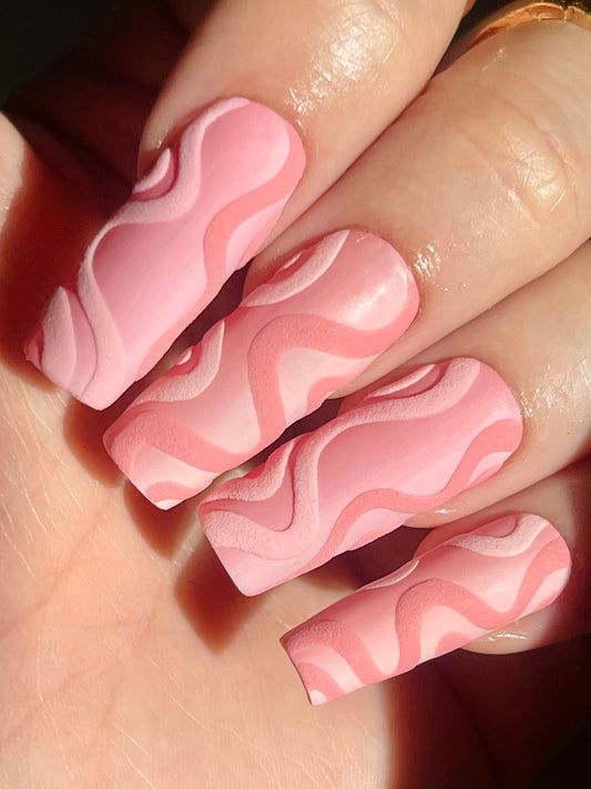 Close-up of a hand with pink and white wavy nail art.