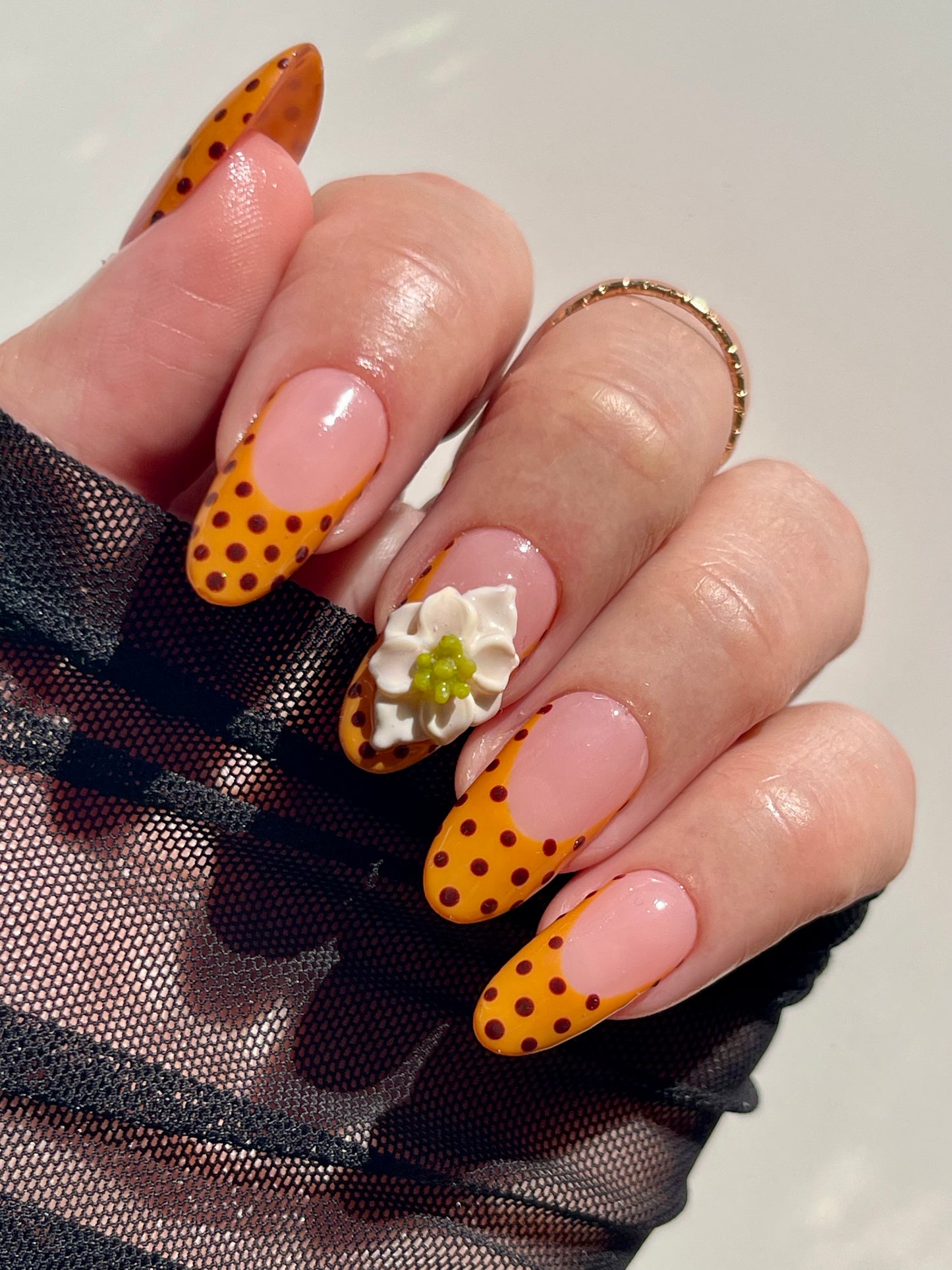 Nail art with orange and black polka dots on a light background