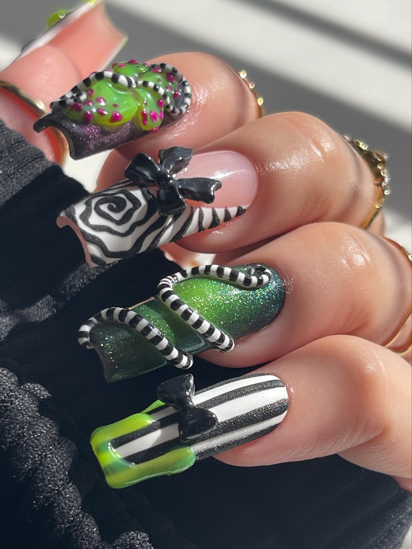 Close-up of a hand with creatively designed nails featuring green, black, and white patterns.