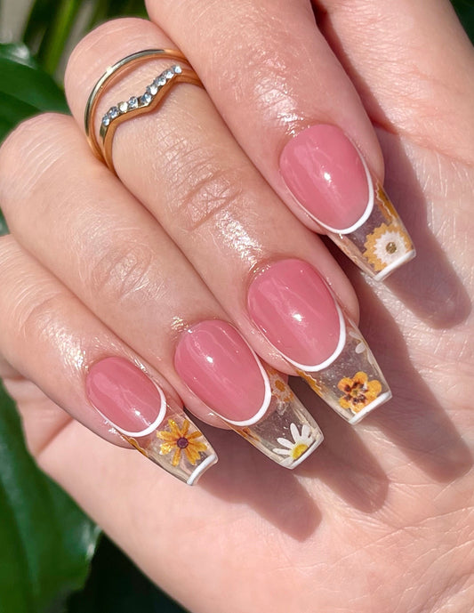 Hand with pink nails featuring floral designs against a green leafy background