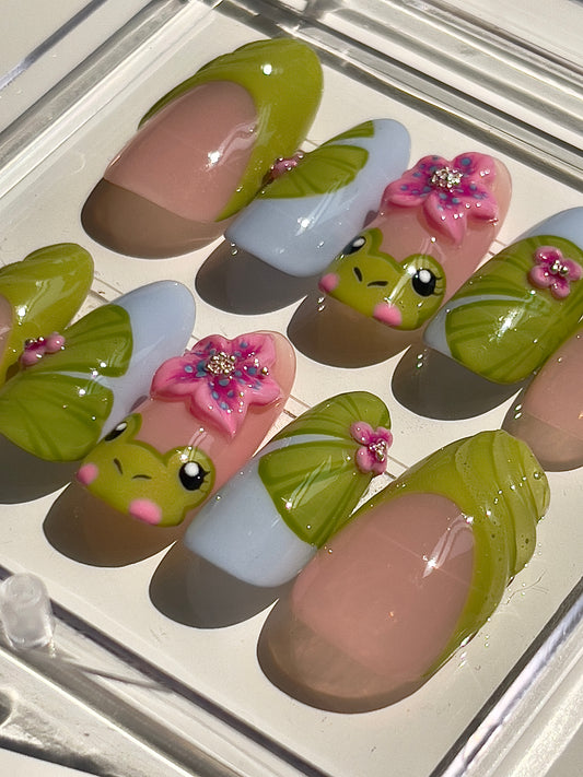 Nail art with frog and flower designs on a clear background
