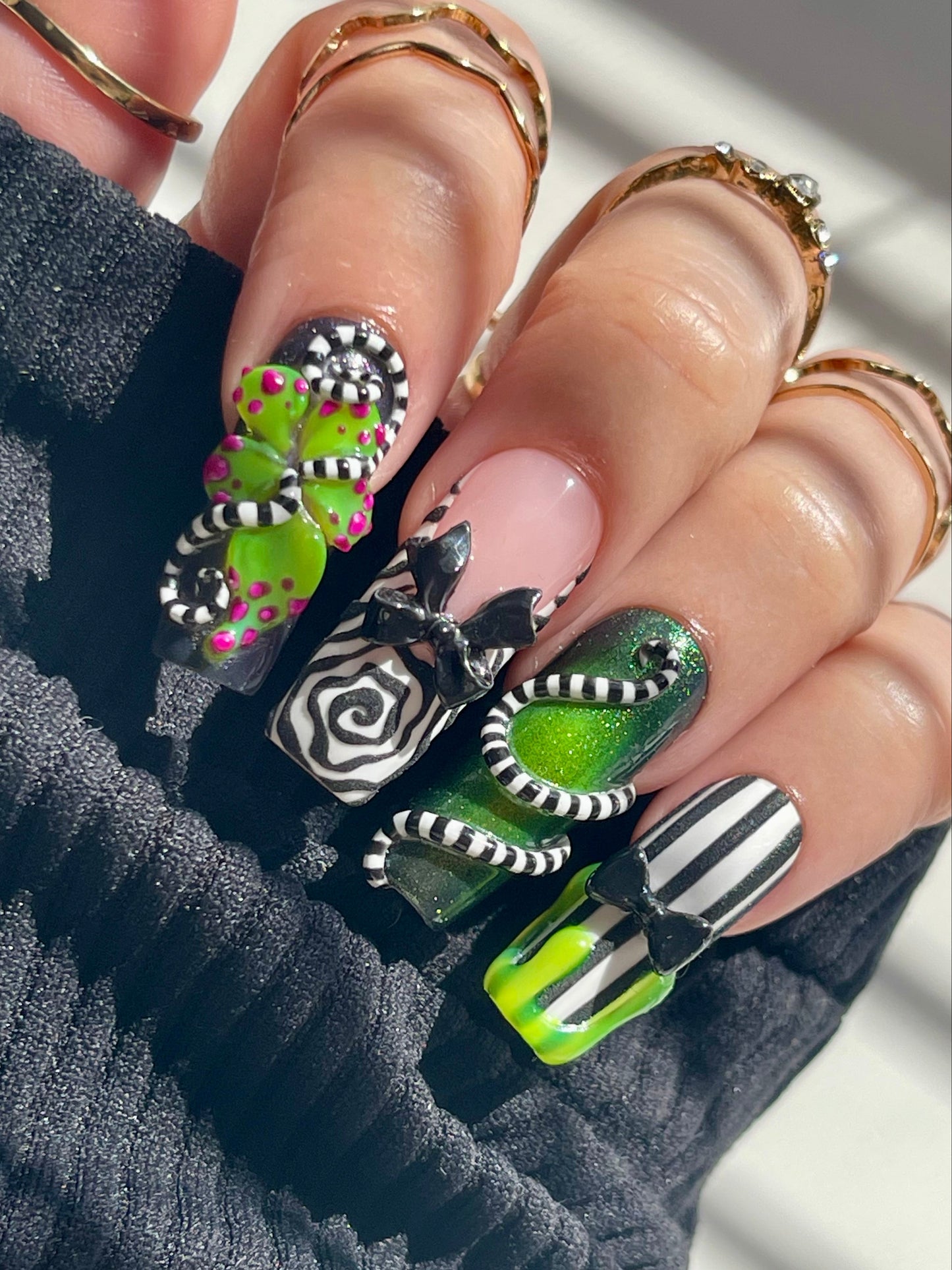 Close-up of a hand with colorful nail art featuring green, black, and white designs.