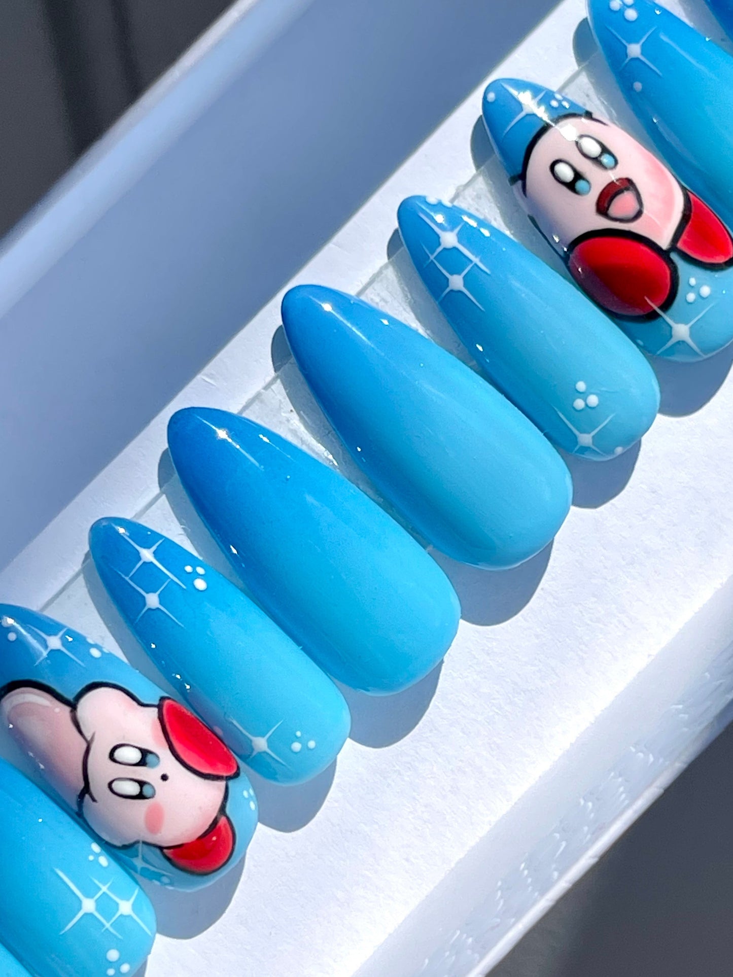Blue ombre nails with cartoon character designs on a white tray.