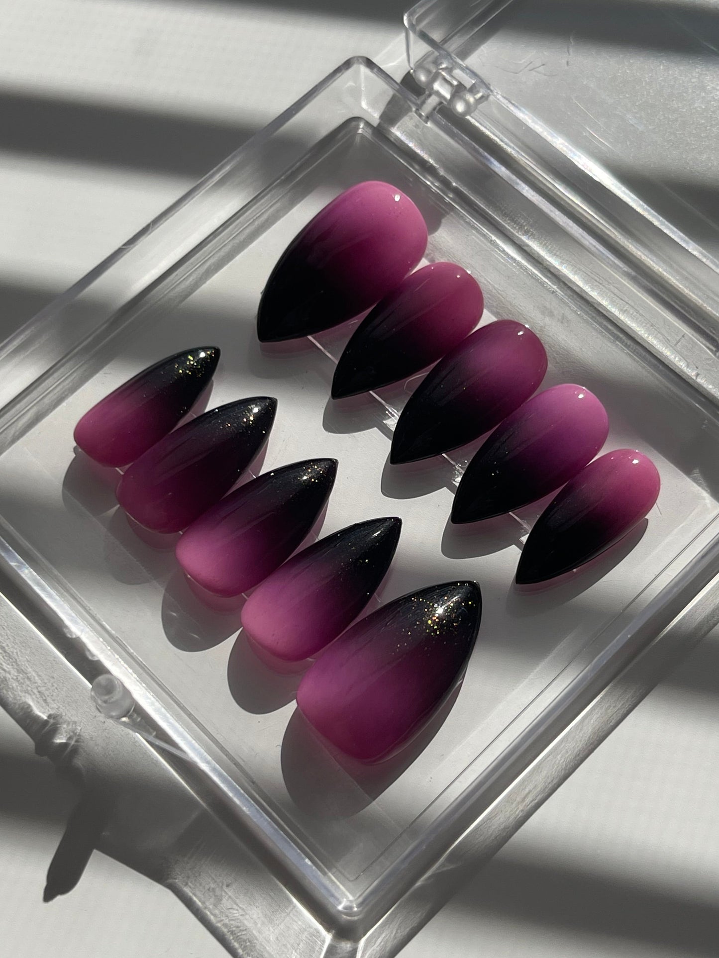 Purple and black nail tips in a clear case on a white background