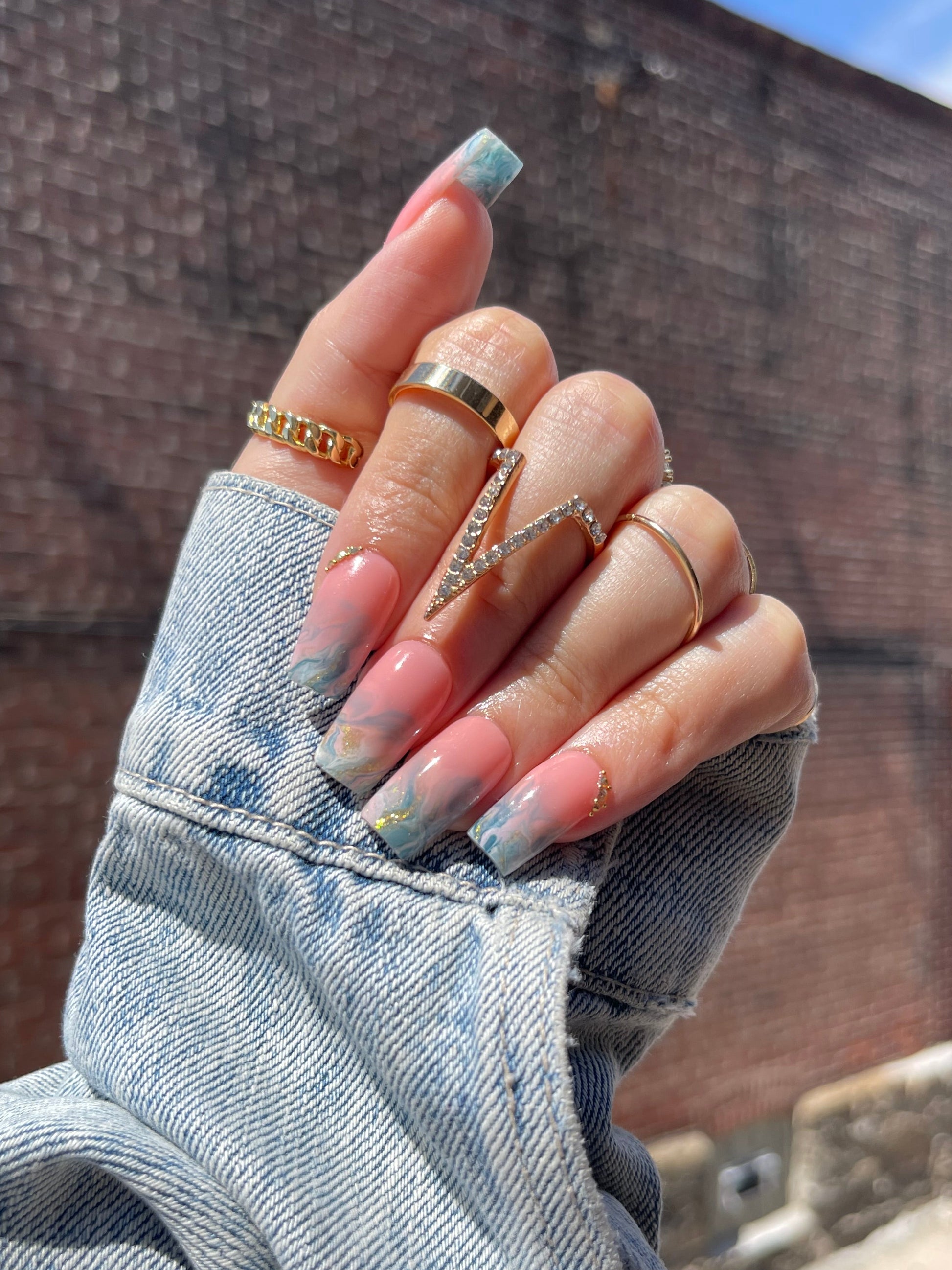 Hand with painted nails and multiple rings on a textured surface
