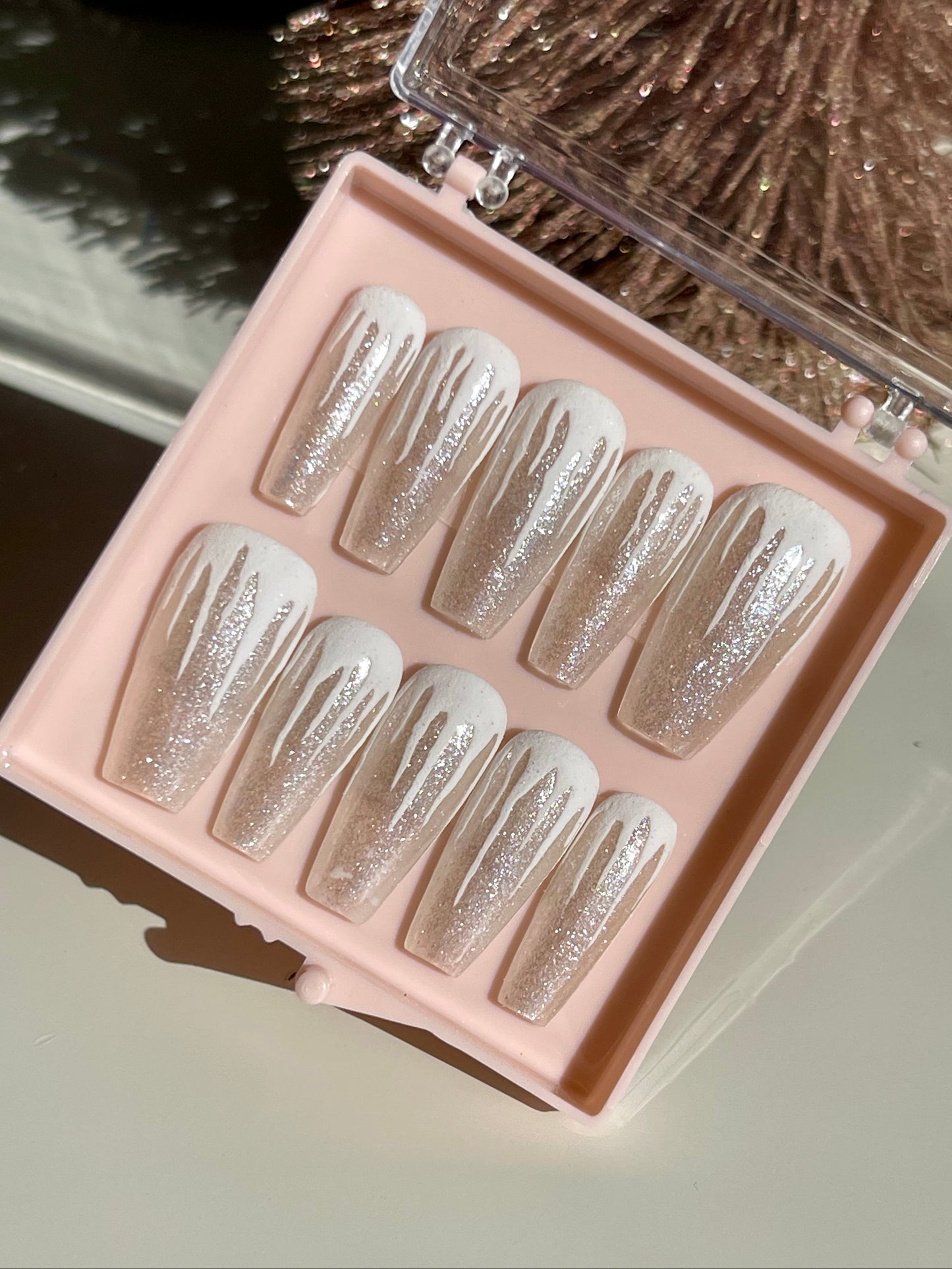 Set of glittery press-on nails in a pink case with a decorative background.
