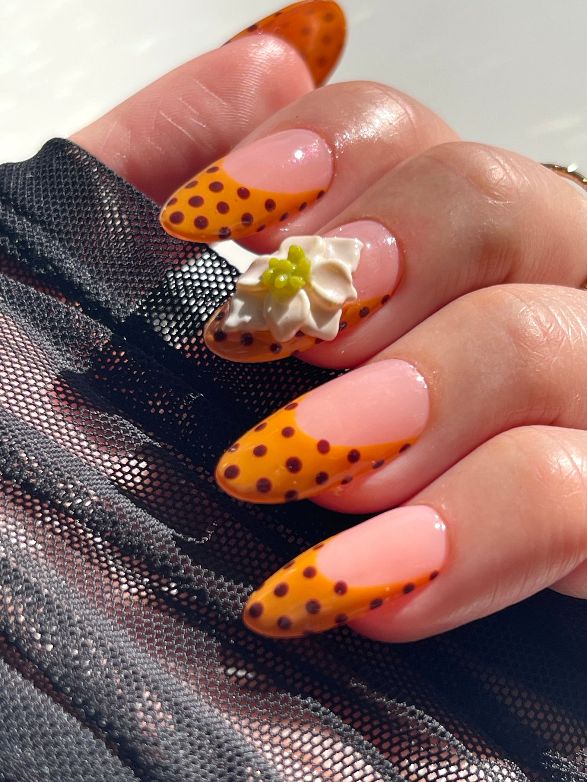 Hand with orange and black polka dot nails and floral decorations.