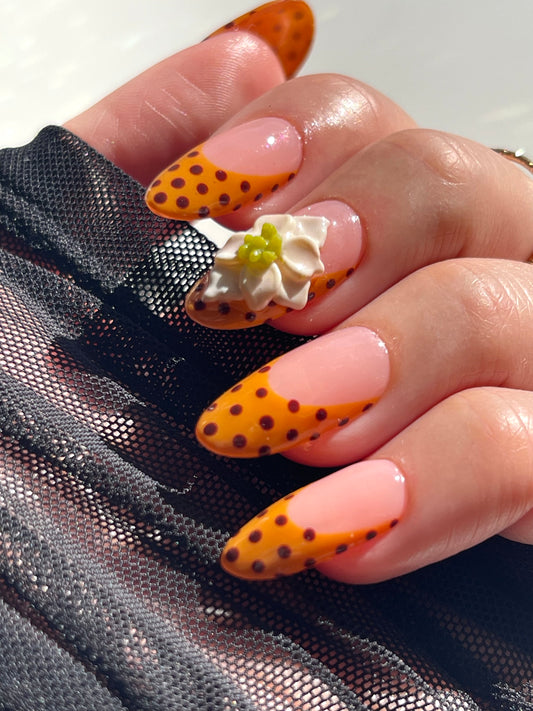 Hand with orange and black polka dot nails and floral decorations.