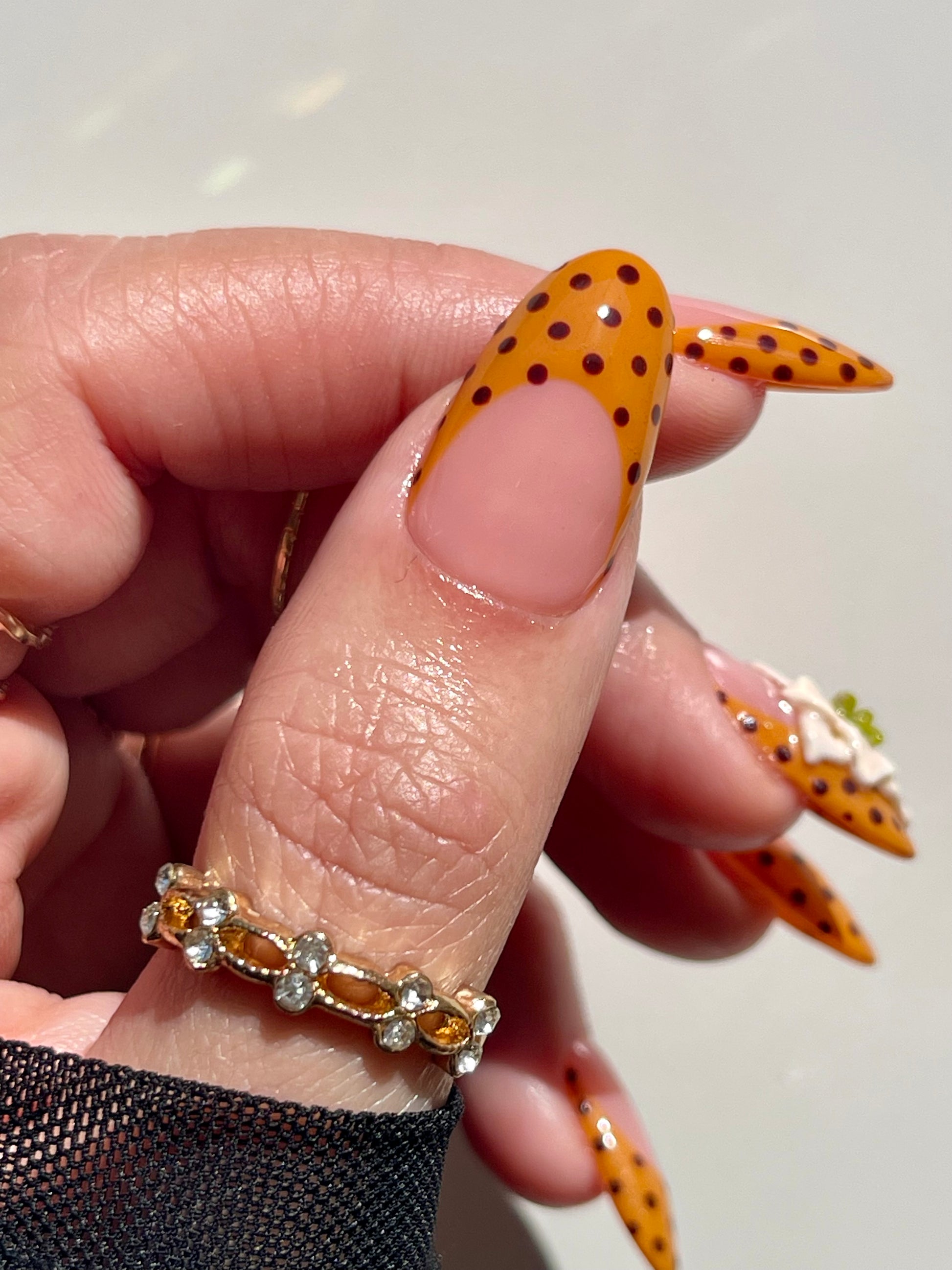 Hand wearing a gold ring with orange gemstones against a neutral background