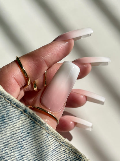 Close-up of a hand with long, white-accentuated nails wearing gold rings on a neutral background