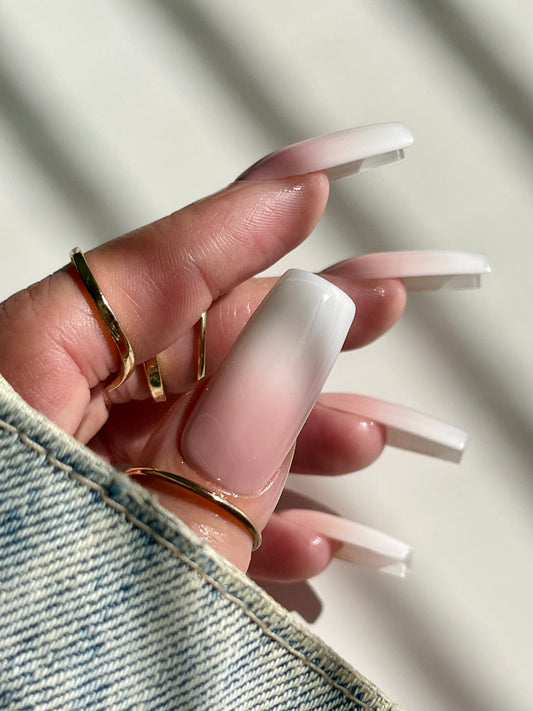 Close-up of a hand with long, white-accentuated nails wearing gold rings on a neutral background