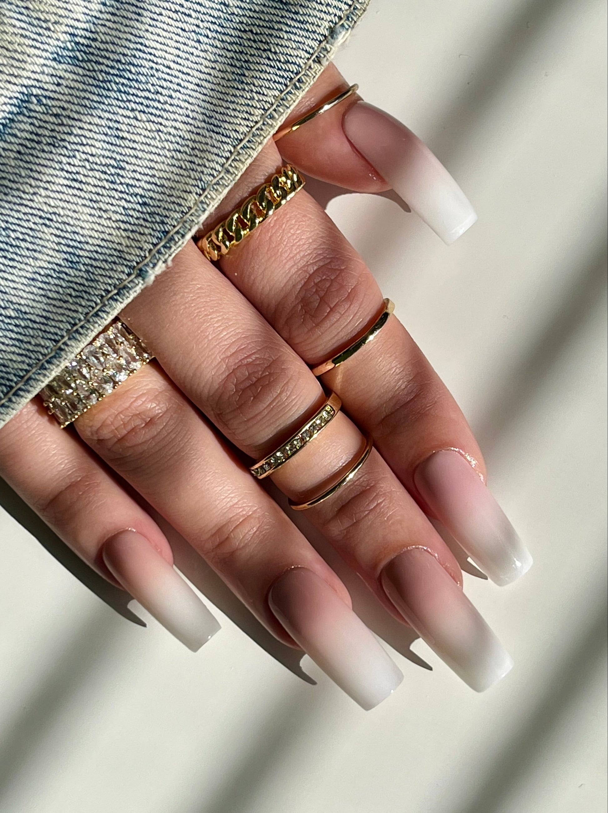 Hand with long, gradient nails wearing multiple rings on a neutral background