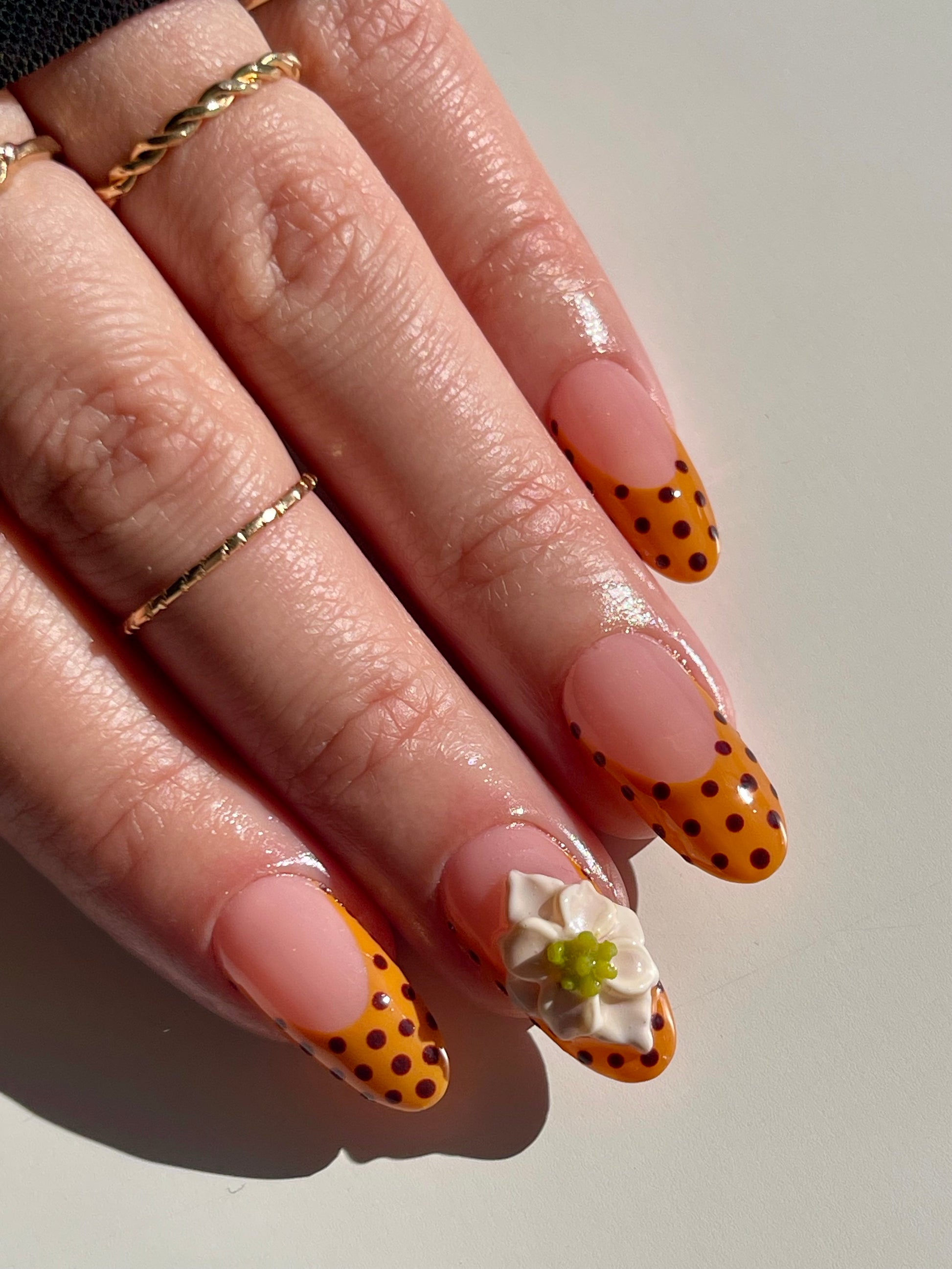 Hand with polka dot nail design and gold rings on a neutral background