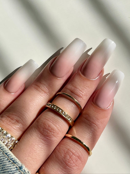 Hand with gradient nail polish and multiple rings on a neutral background