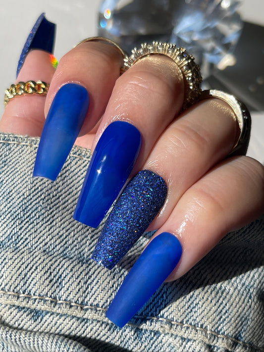 Hand with blue nail polish wearing a gold ring on a denim background