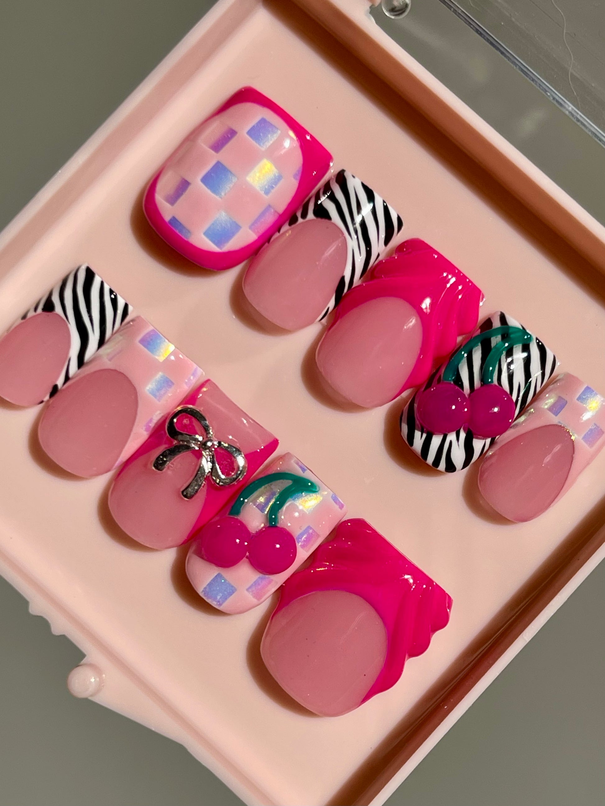 Set of decorative false nails with pink and zebra patterns on a pink tray.