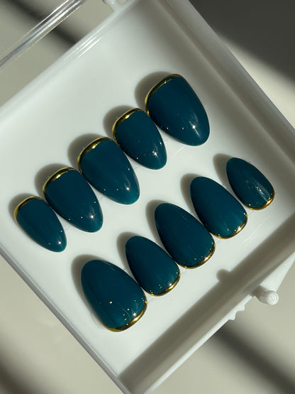 Set of blue nail extensions with gold tips on a white tray.
