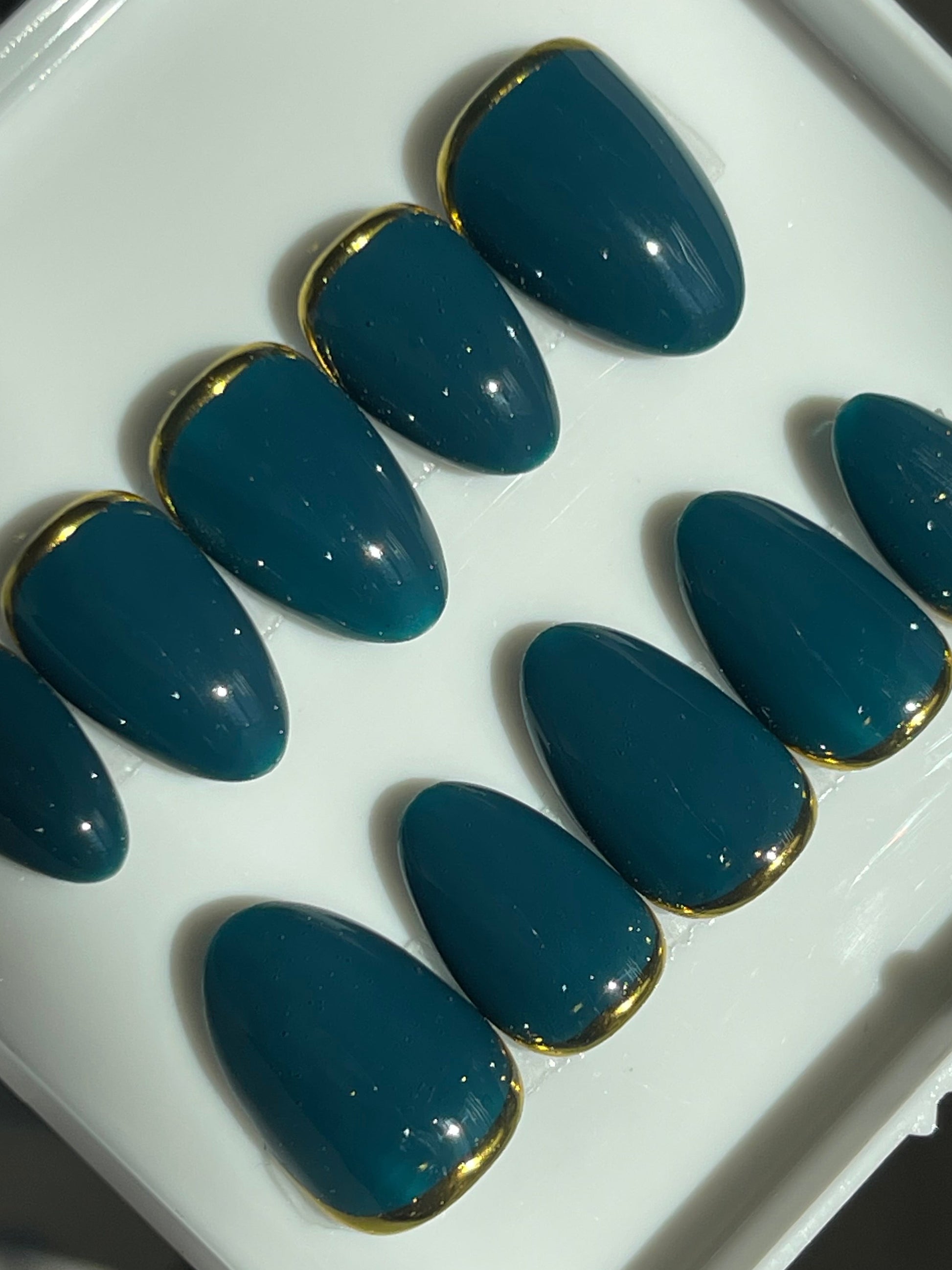 Set of blue nail extensions with gold tips on a white tray.