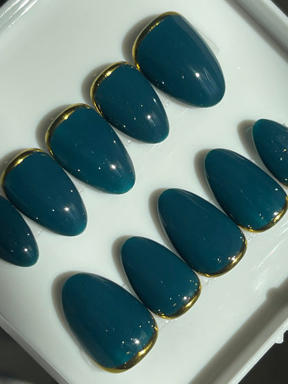 Set of blue nail extensions with gold tips on a white tray.