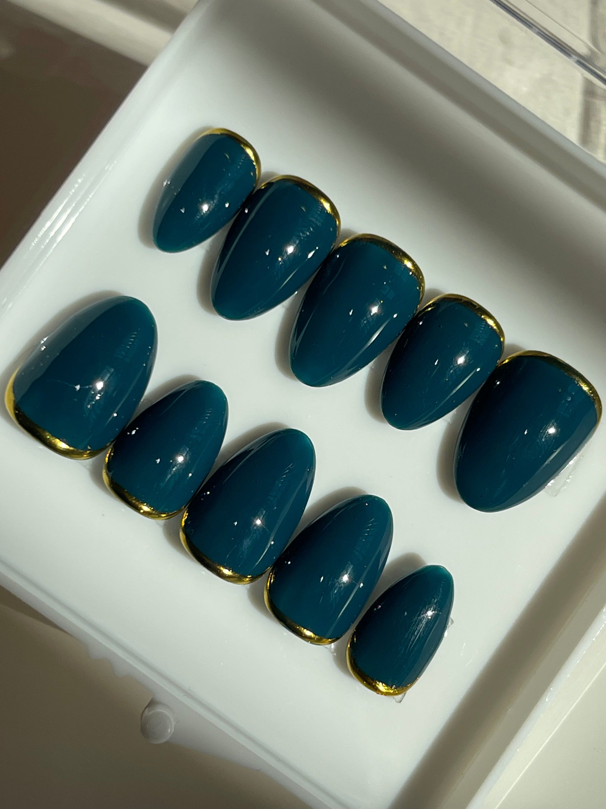 Set of blue nail extensions with gold tips on a white tray