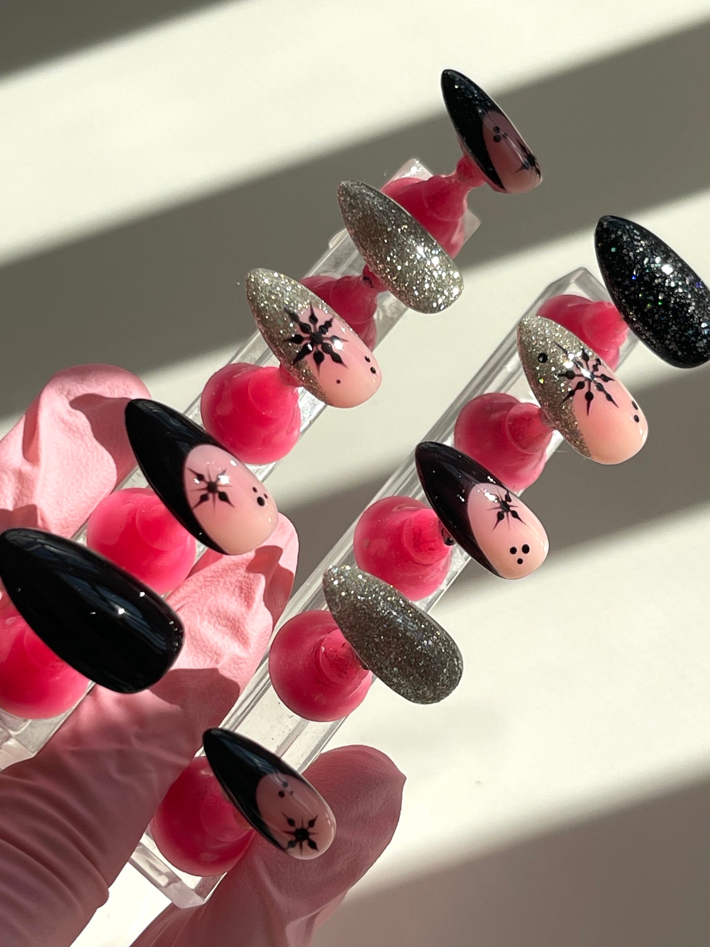 Set of false nails with black, pink, and glittery designs held in a clear stand.