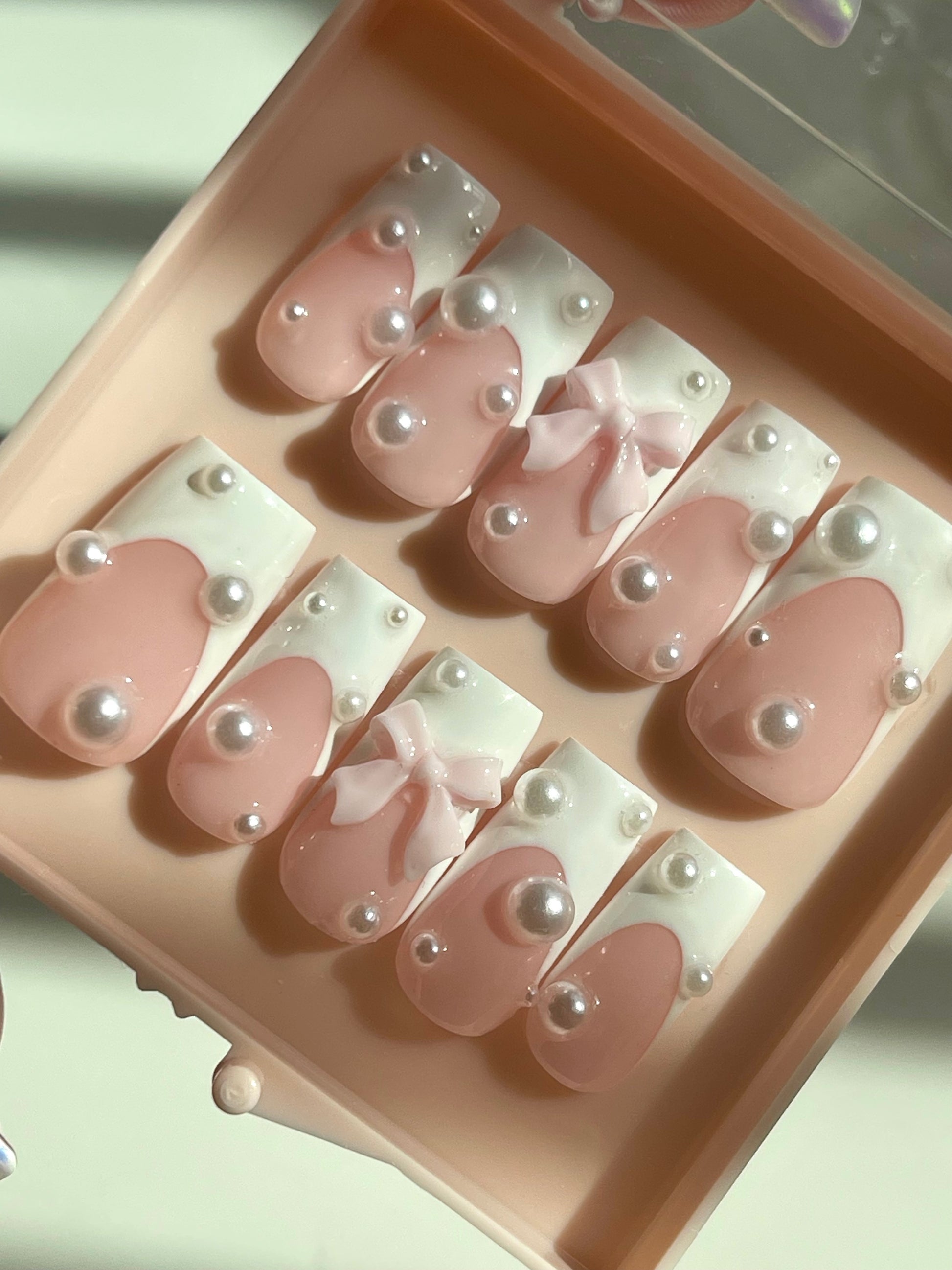 Set of pink and white nail designs with pearls in a pink case.