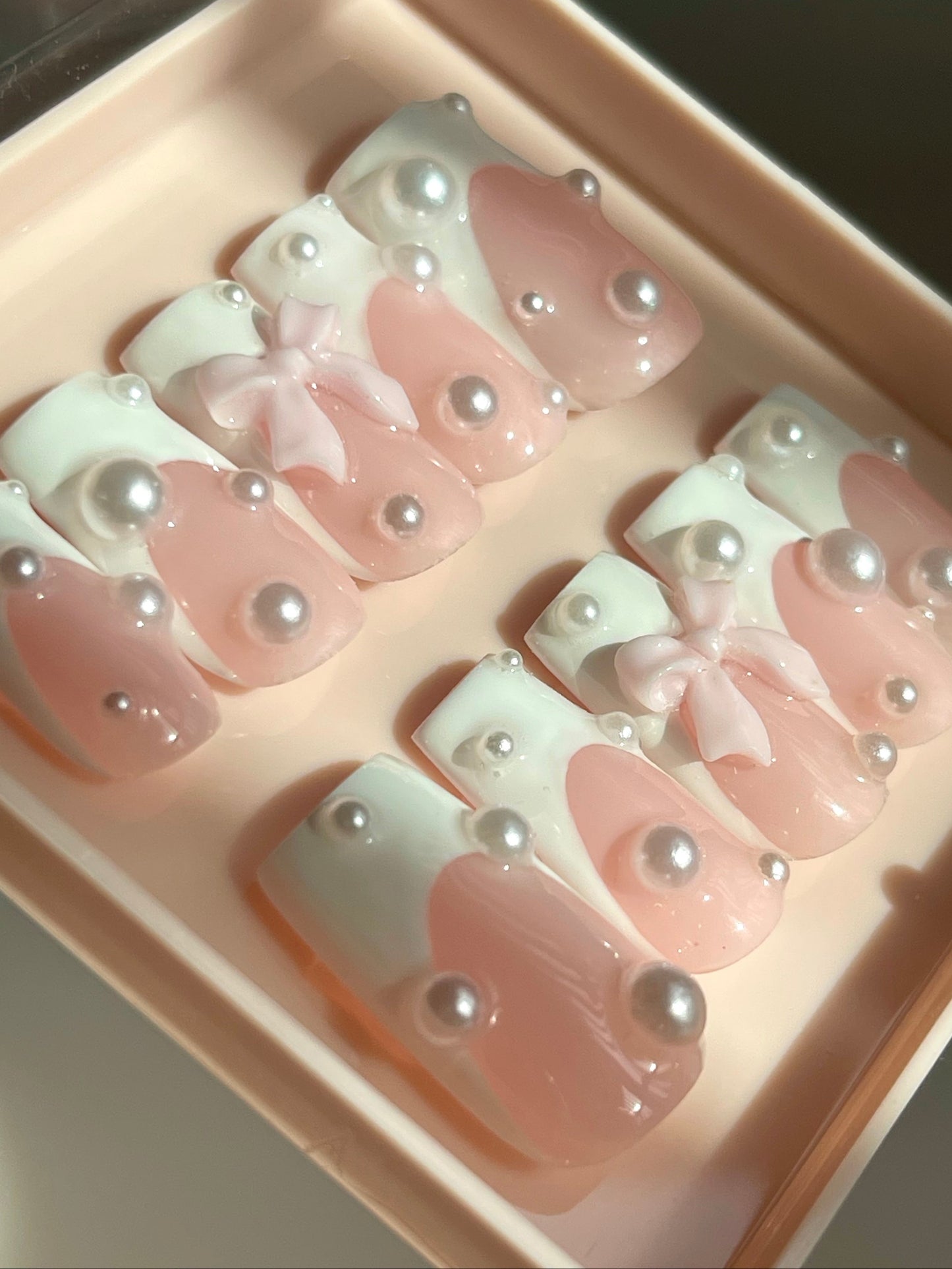 Set of pink and white nail designs with bows and pearls in a box.