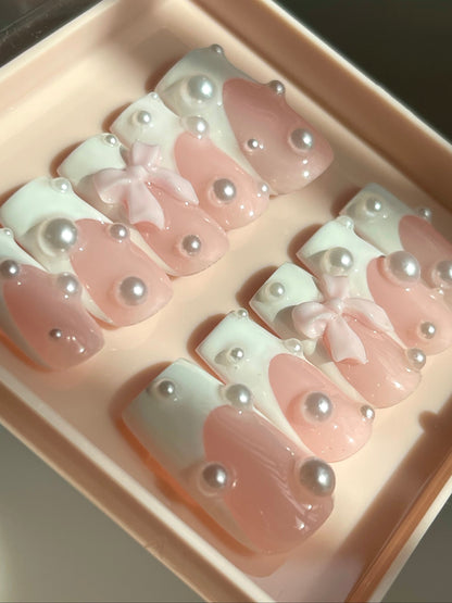 Set of pink and white nail designs with bows and pearls in a box.