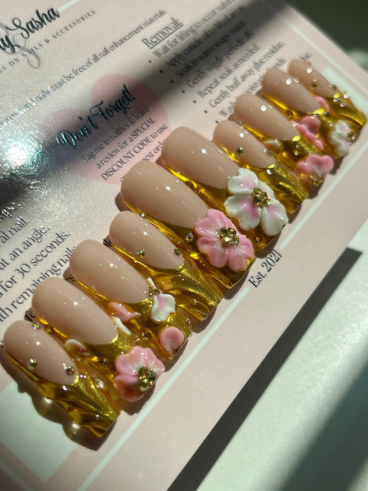 Nail art display with beige nails decorated with pink flowers and gold accents on a white surface.