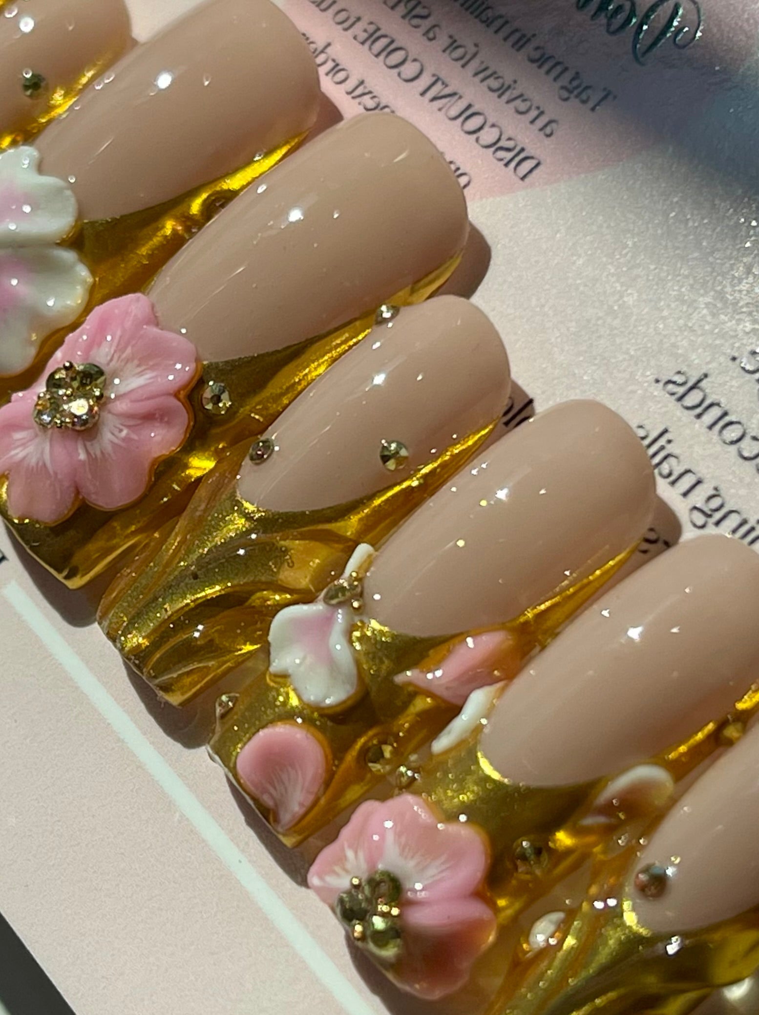Nail art display with beige nails decorated with pink flowers and gold accents on a display card