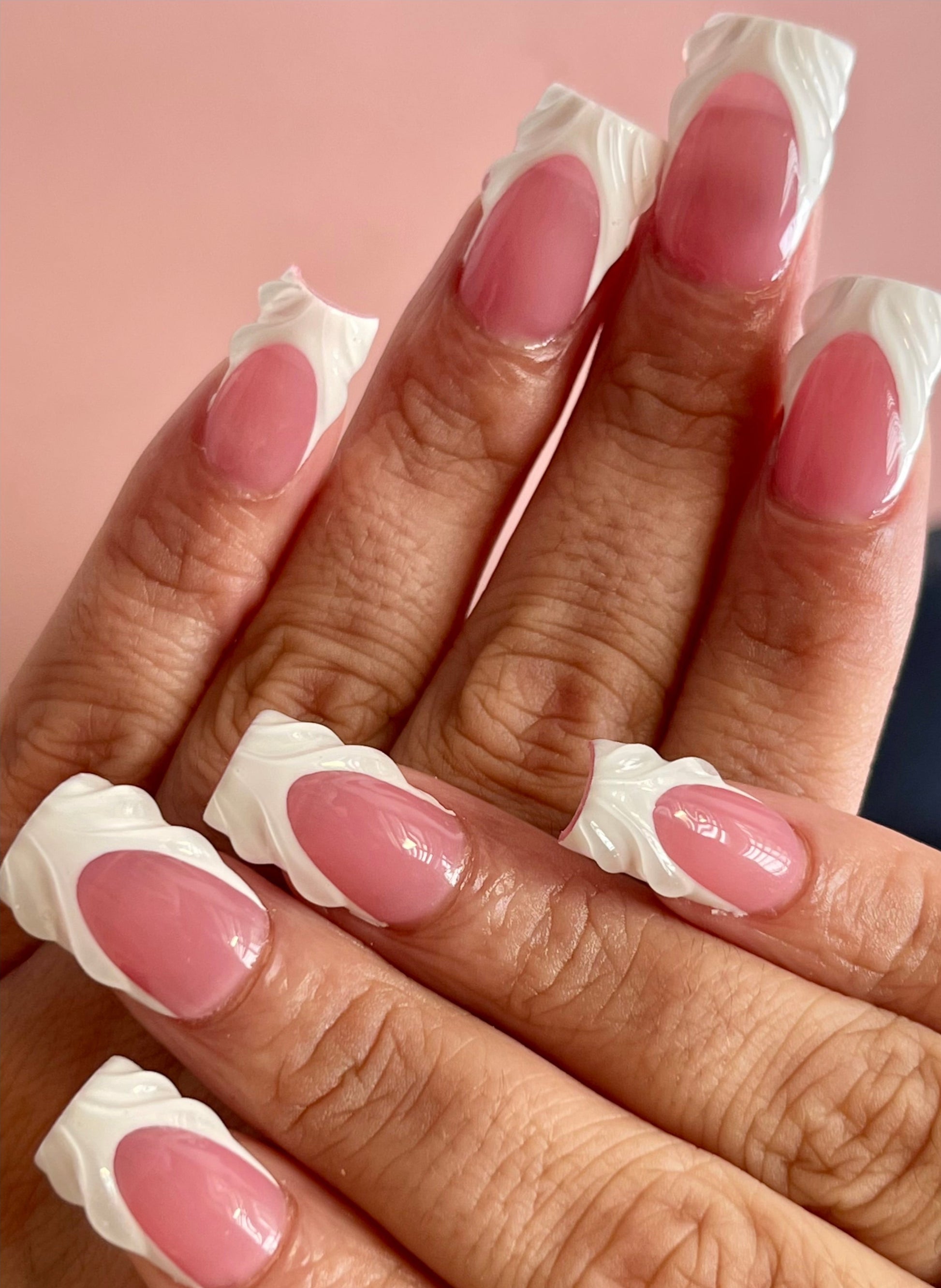 Close-up of hands with pink nail polish and white tips on a pink background