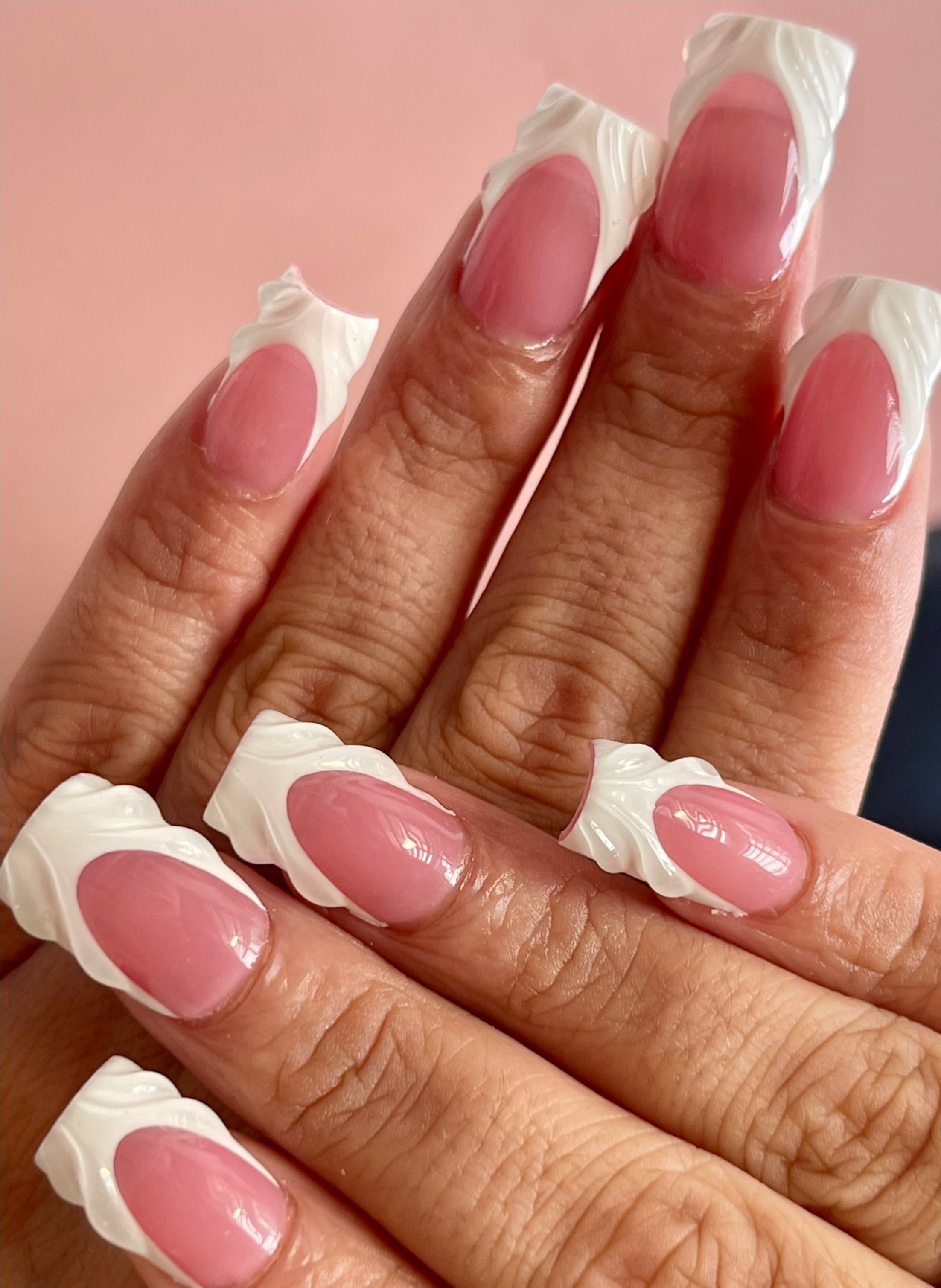 Close-up of hands with pink nail polish and white tips on a pink background