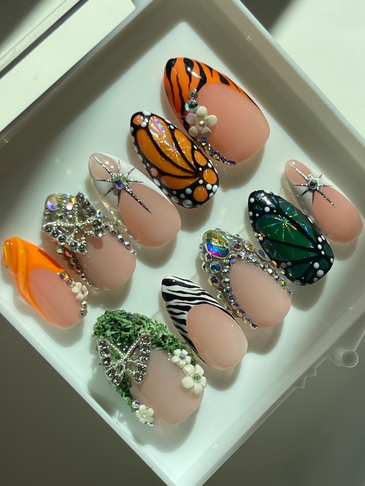 Decorative nail art with butterfly and nature-themed designs on a white surface.