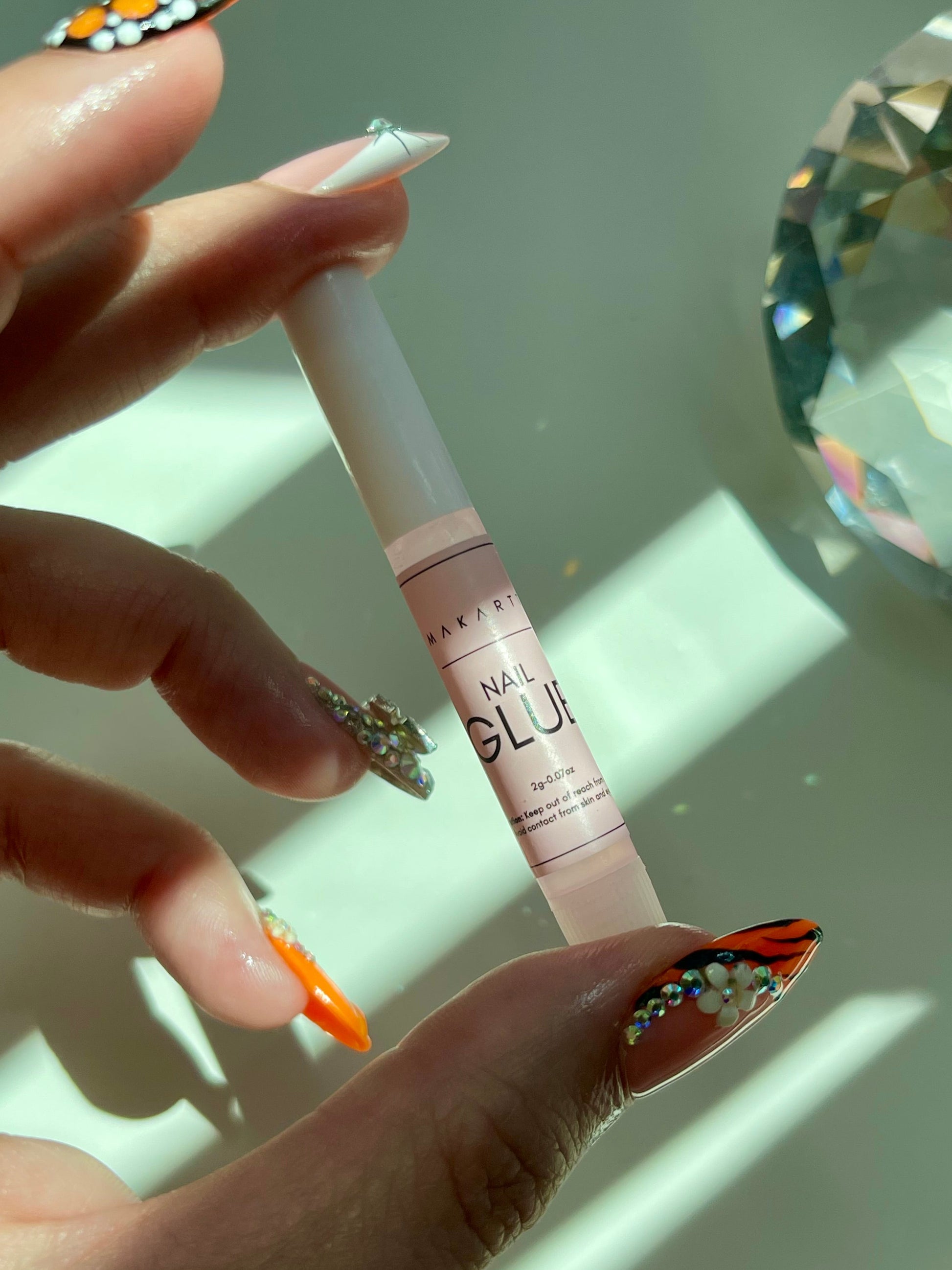 Hand holding a bottle of Maybelline nail glue with decorative nails.