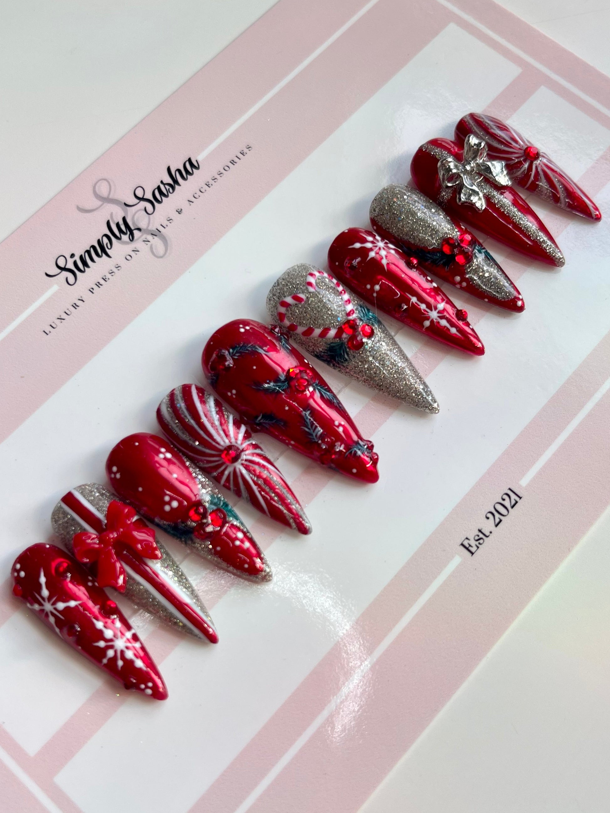 Decorative false nails with red and silver design on a Simply Sasha branded tray.