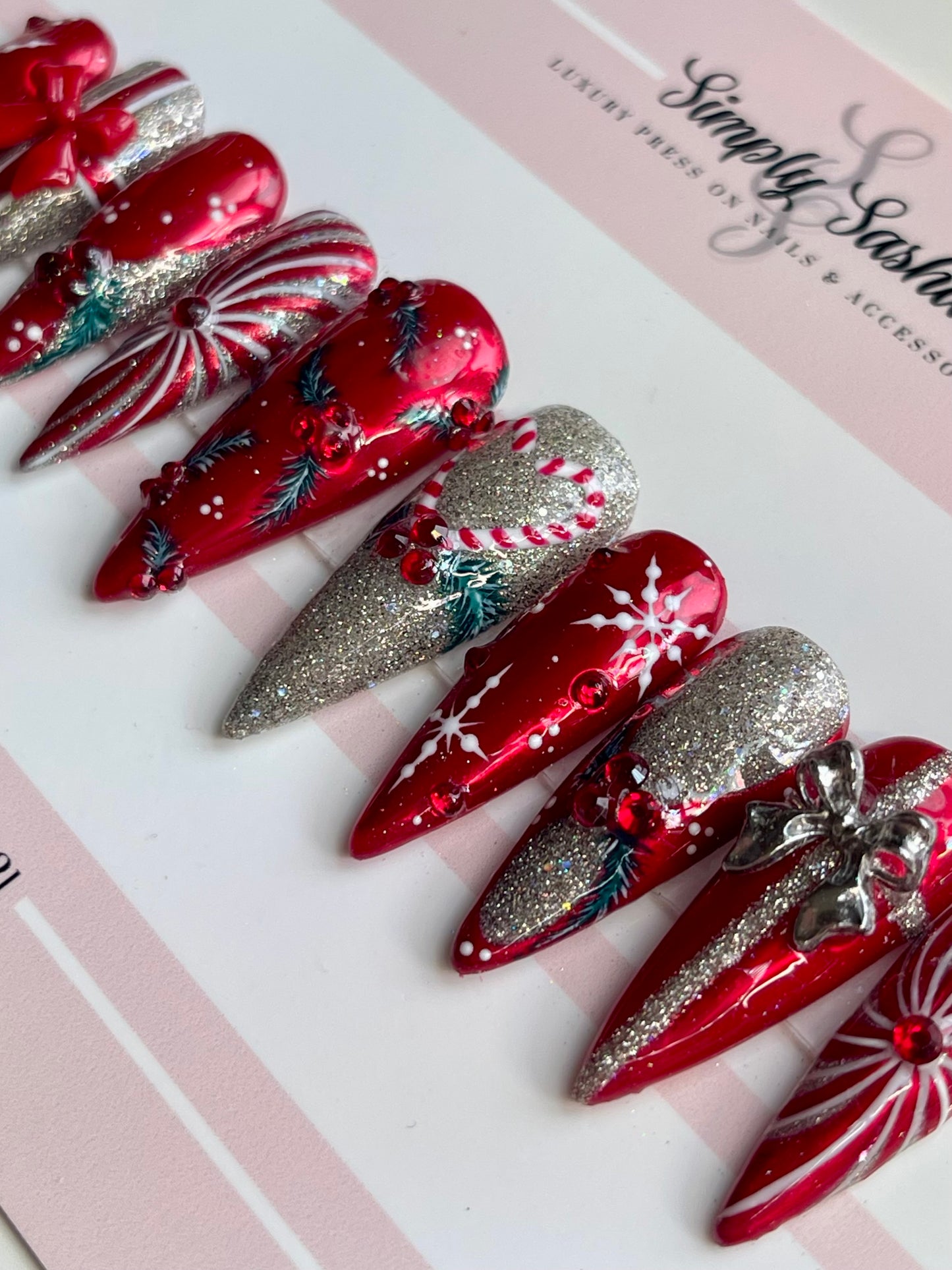 Decorative red and silver nails on a white surface with Simply Sasha branding.