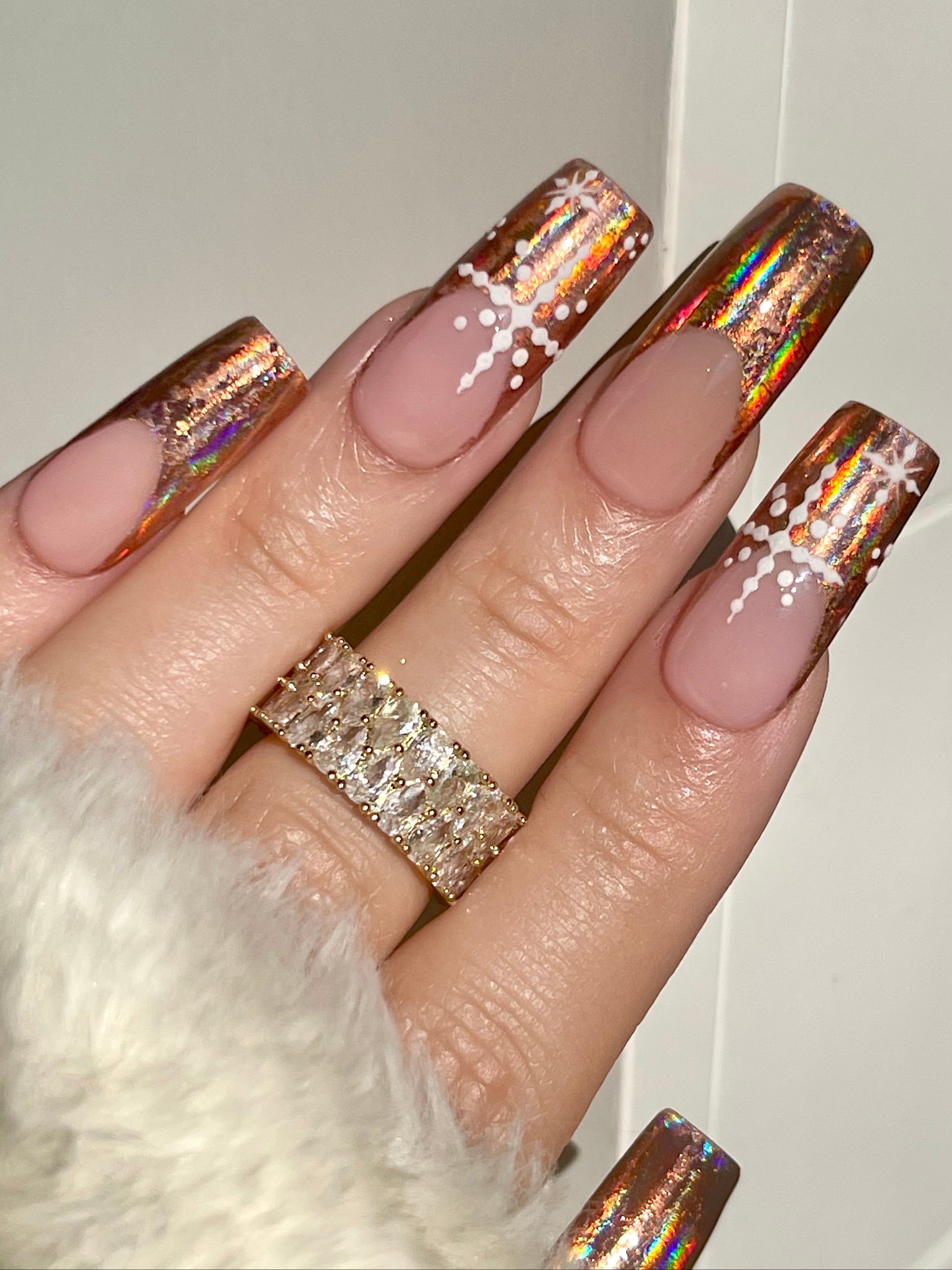 Hand with pink nails and glittery gold tips, wearing a diamond ring, against a neutral background.