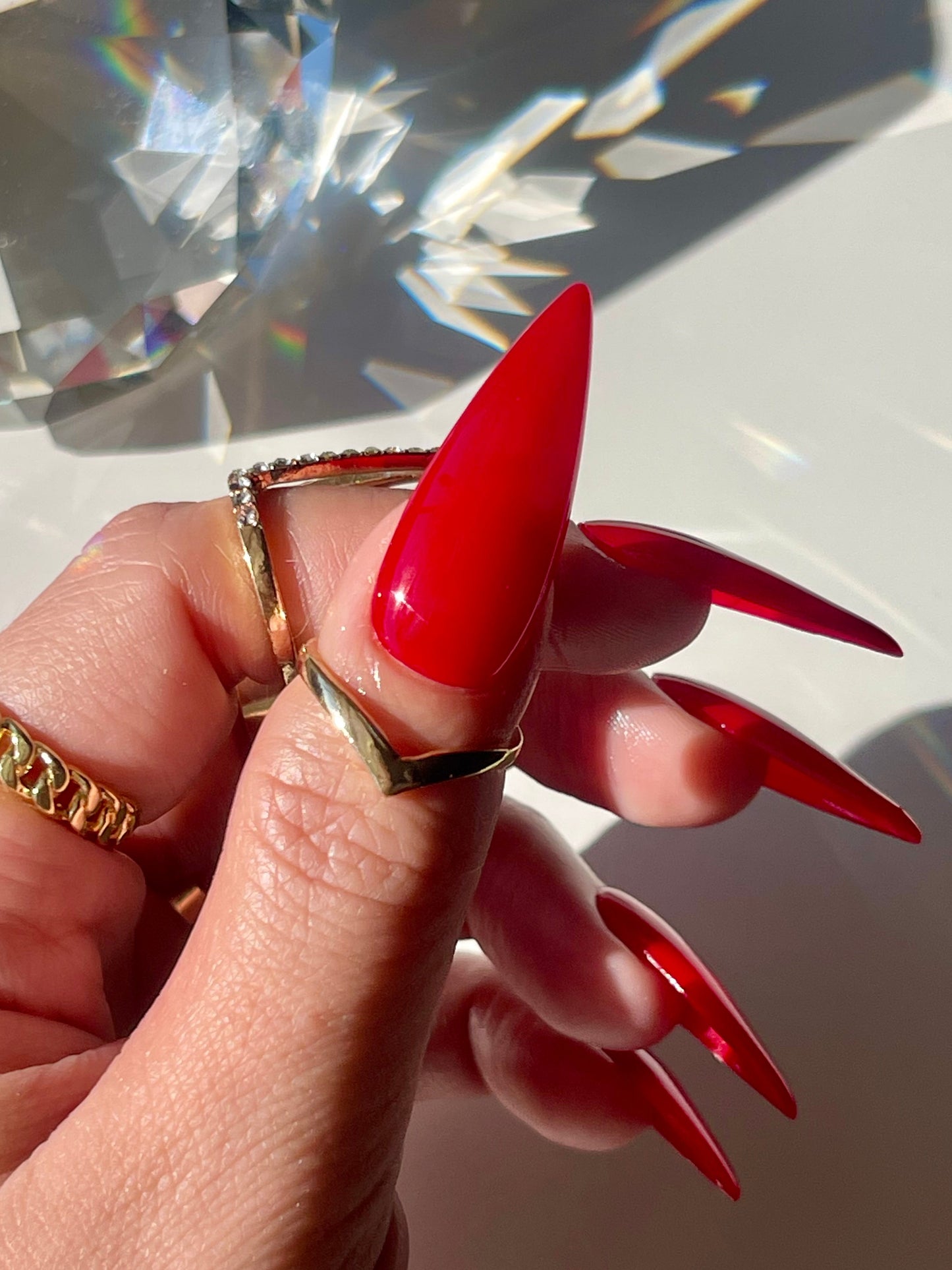Hand with red nail polish wearing gold rings on a reflective surface