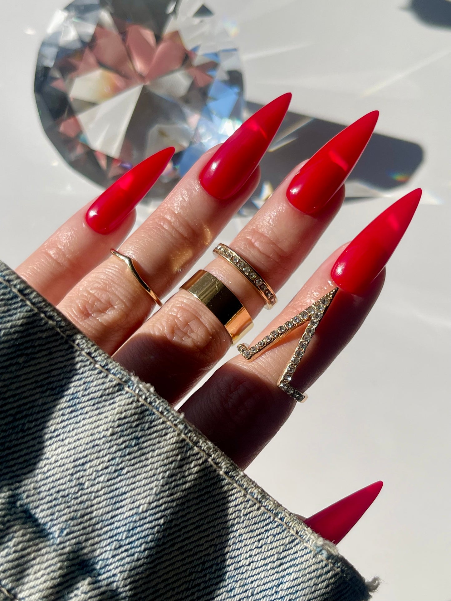 Hand with red stiletto nails and gold rings on a white background