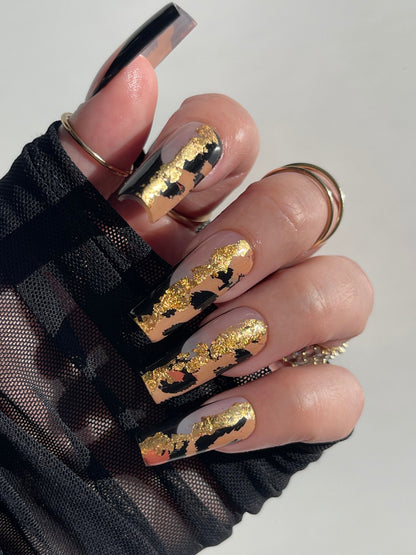 Nails with gold and black designs on a neutral background
