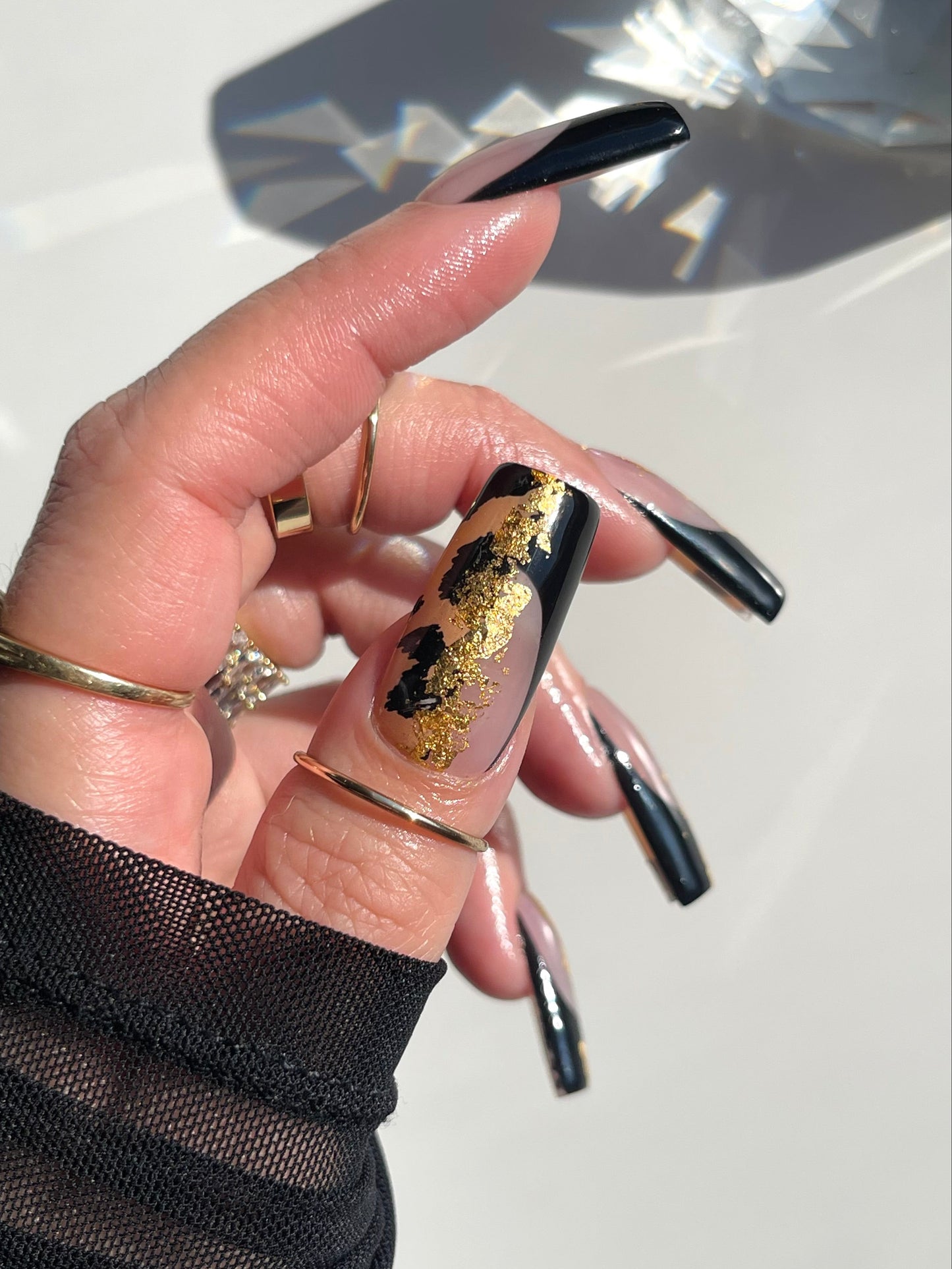 Hand with black and gold nail design wearing a gold ring on a light background