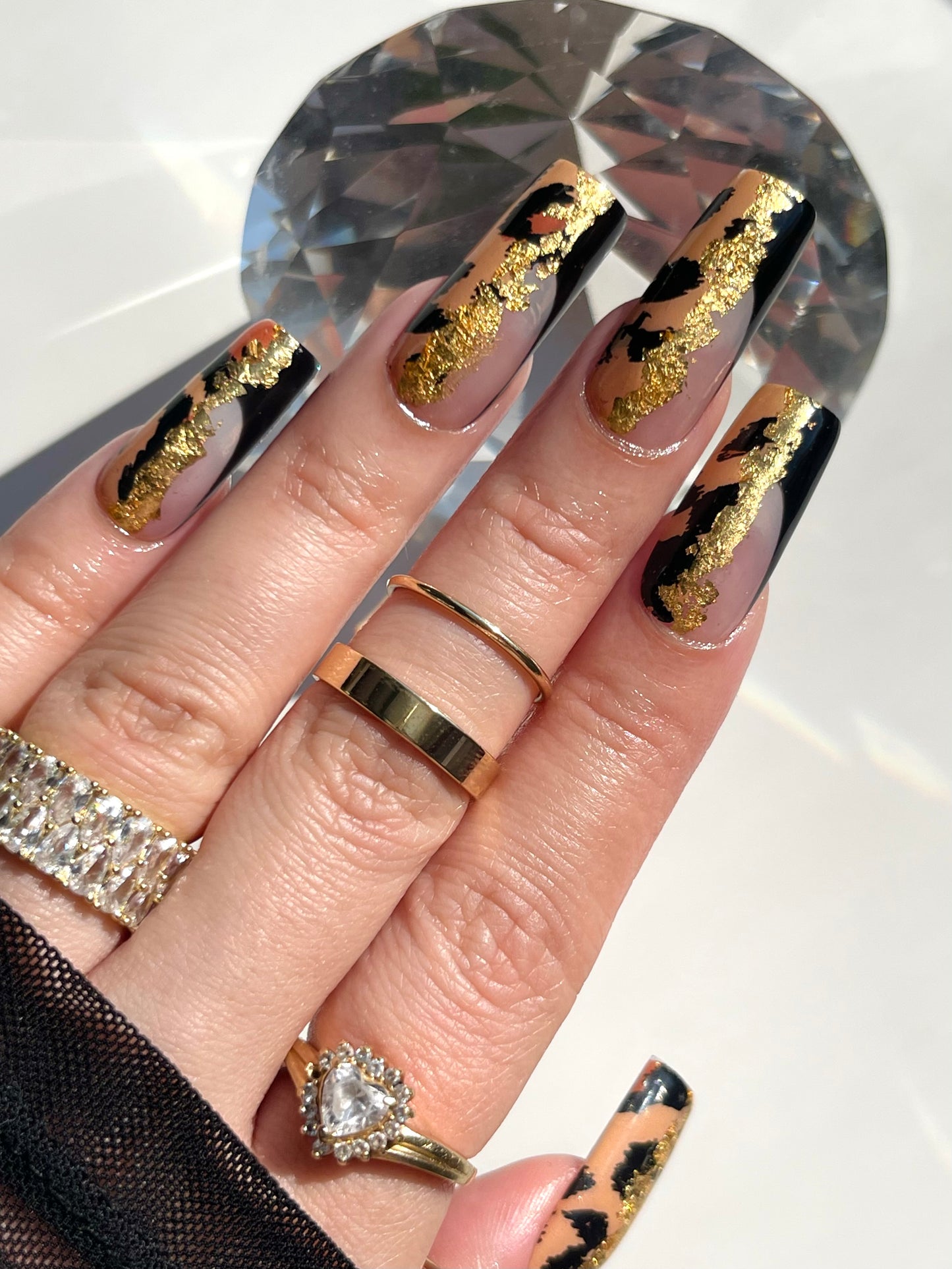 Hand with gold and black nail design wearing multiple rings on a reflective surface