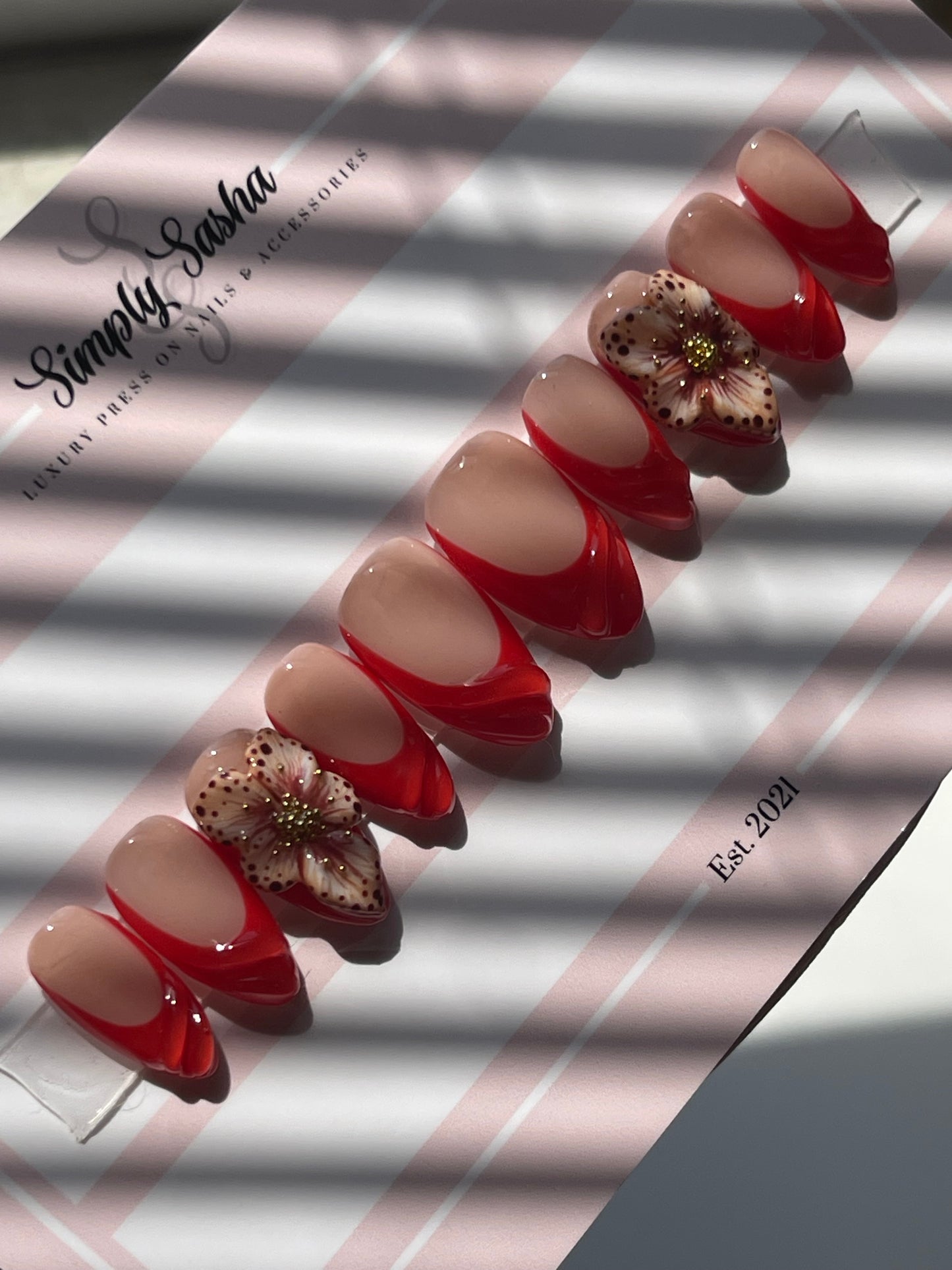 Nail art display with red and beige designs on a striped background