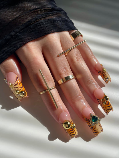 Hand with gold rings and tiger nail designs on a neutral background