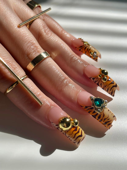 Hand with gold rings and tiger nail designs on a neutral background