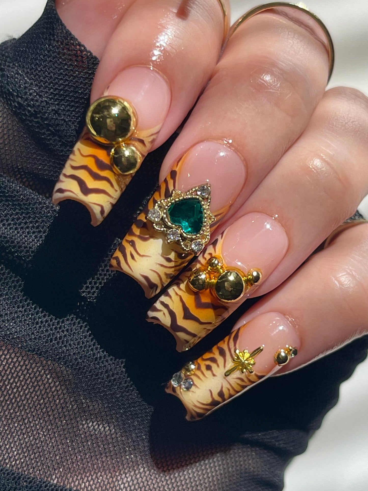 Nails with tiger stripe design and gemstone decorations on a neutral background