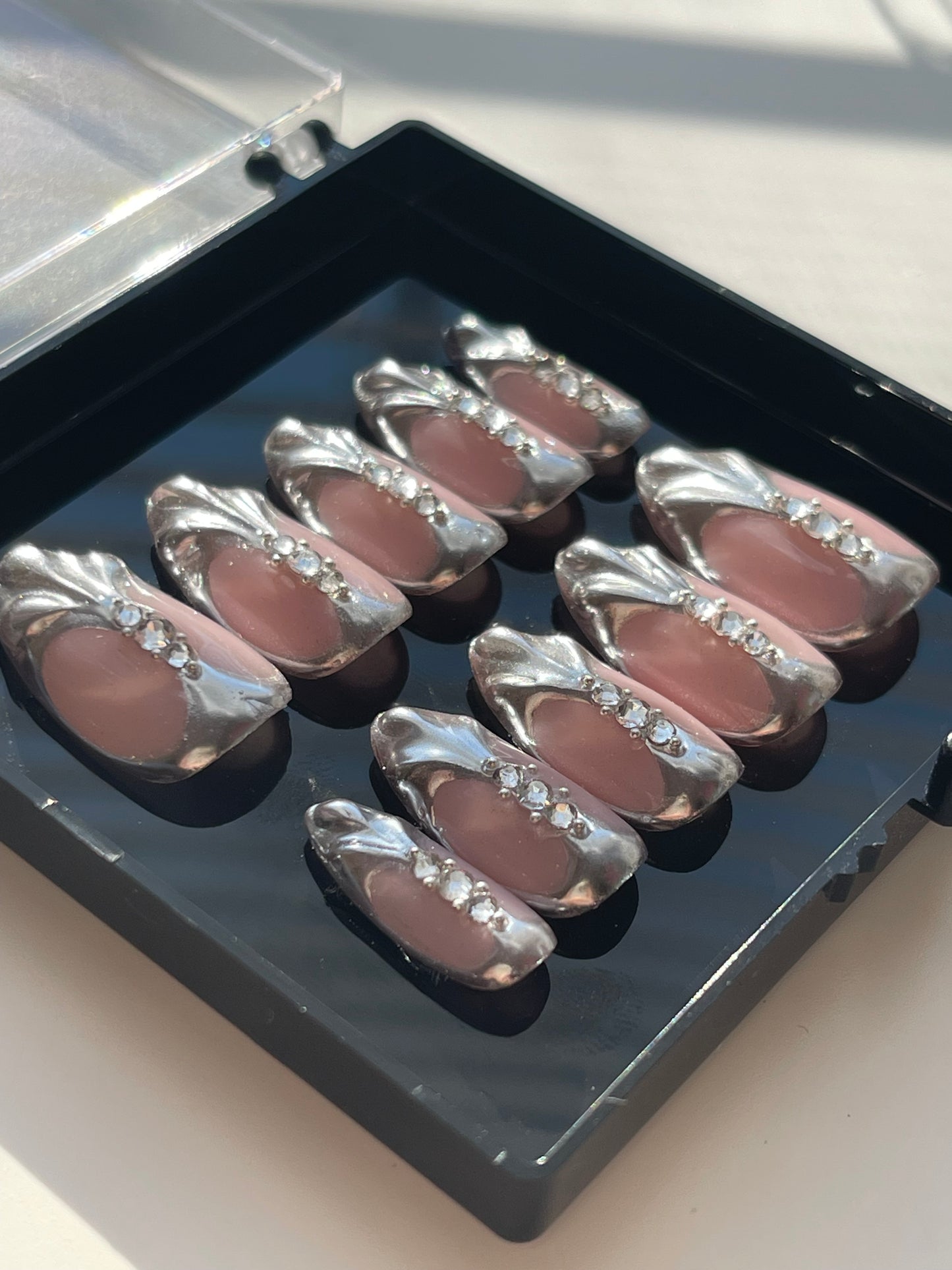 Set of false nails with rhinestones in a clear case on a light background