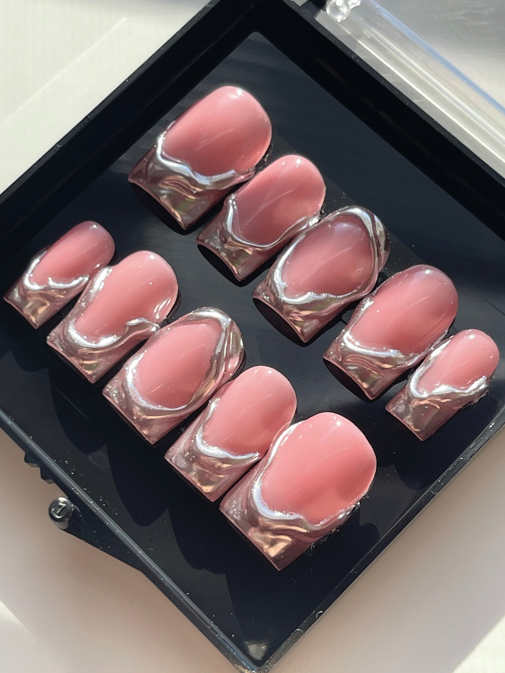 Set of pink nail pads with silver swirl design in a black case.
